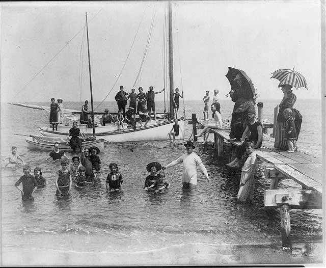 [Men, women, and children in bathing suits on dock, sailboats, and in…, 1880